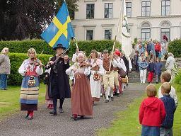KF marscherar med flaggor till
                fiolmusik ned till dansplatsen vid Karlslunds
                Herrg&aring;rd